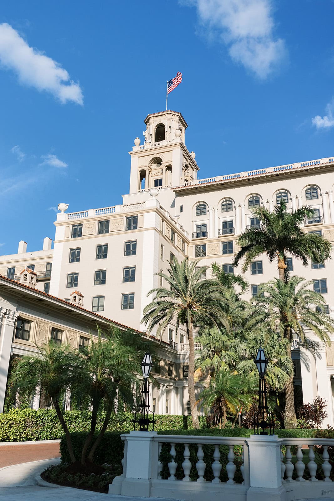 Front facade of The Breakers wedding venue in Palm Beach flying the american flag with palm trees in the foreground