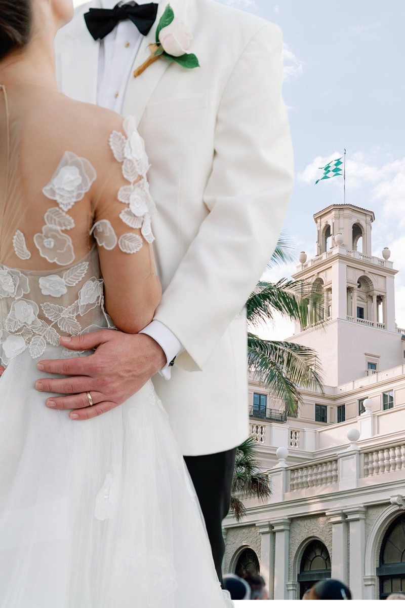 bride and groom wearing all white in front of the tower of The Breakers